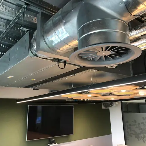 Ceiling-mounted ducted fan coil unit connected to circular supply ductwork in a commercial building.